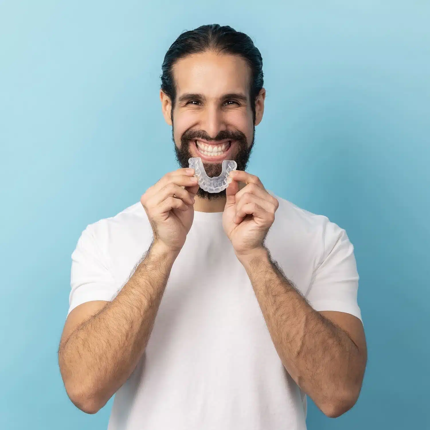 Smiling man holding clear Invisalign aligner against a light blue background, showcasing the comfort and discretion of Invisalign treatment available in Glendale.