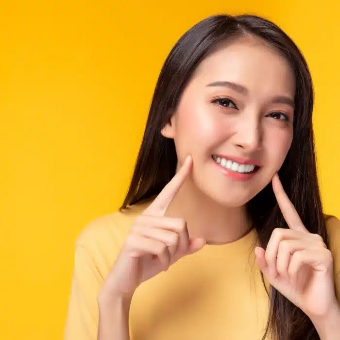 Smiling woman in a yellow shirt pointing at her straight teeth, representing the benefits of Invisalign treatment for a beautiful smile in Eagle Rock, CA.