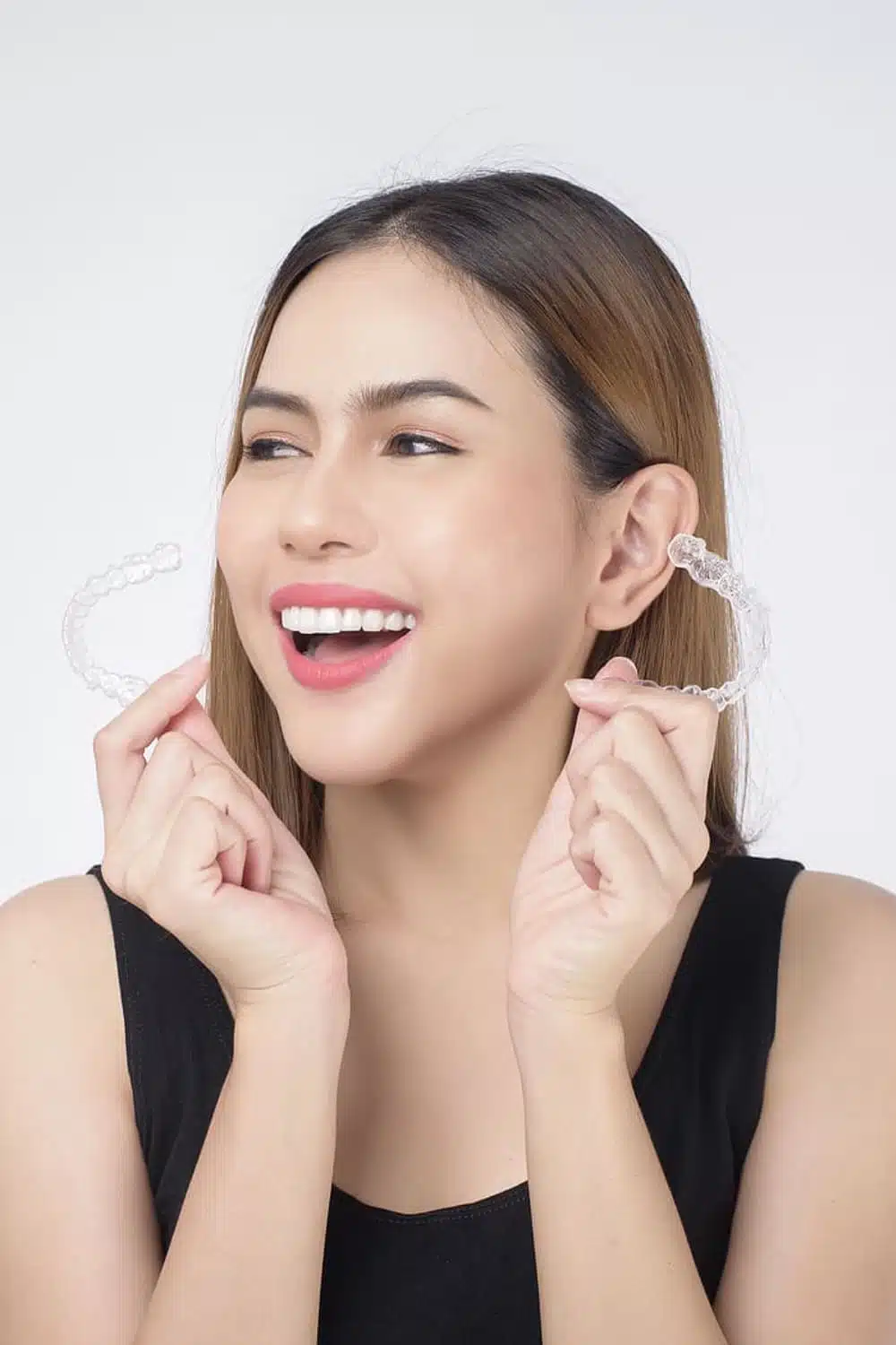 Smiling woman holding clear aligners, showcasing Invisalign as a modern orthodontic solution for teeth straightening.