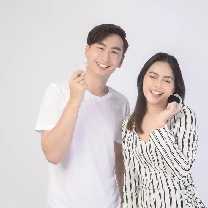Young man and woman smiling while holding clear aligners, representing modern orthodontic treatment options like Invisalign at Eagle Rock Orthodontics in Highland Park.