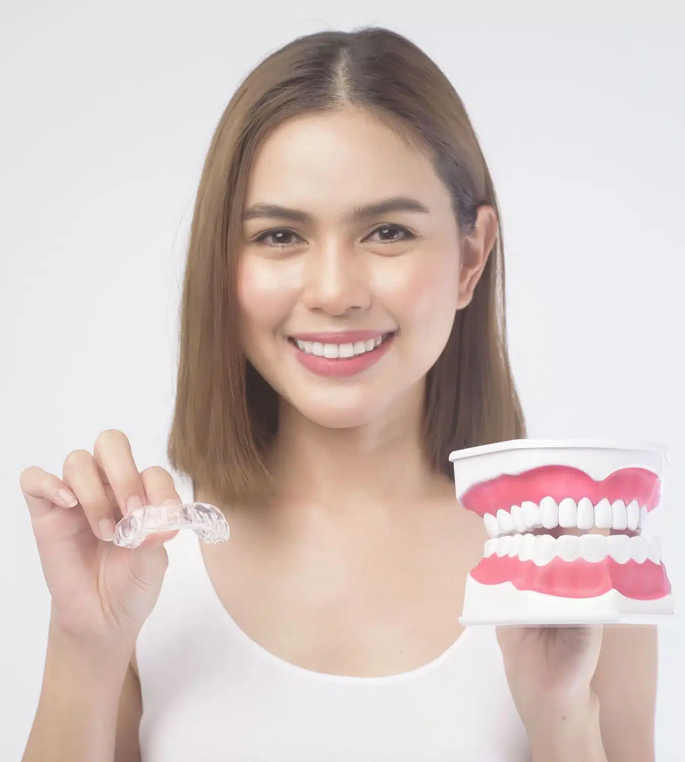 Smiling woman holding clear Invisalign aligner and dental model illustrating orthodontic treatment options for improved bite and oral health.