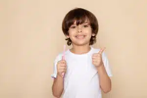 Smiling boy holding a toothbrush and giving a thumbs up, representing confidence in dental health and early orthodontic care.