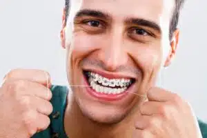 Man smiling with braces while flossing, highlighting adult orthodontics and oral hygiene benefits in Los Angeles.