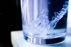 Retainer submerged in water inside a clear glass, illustrating the importance of daily cleaning for orthodontic care.