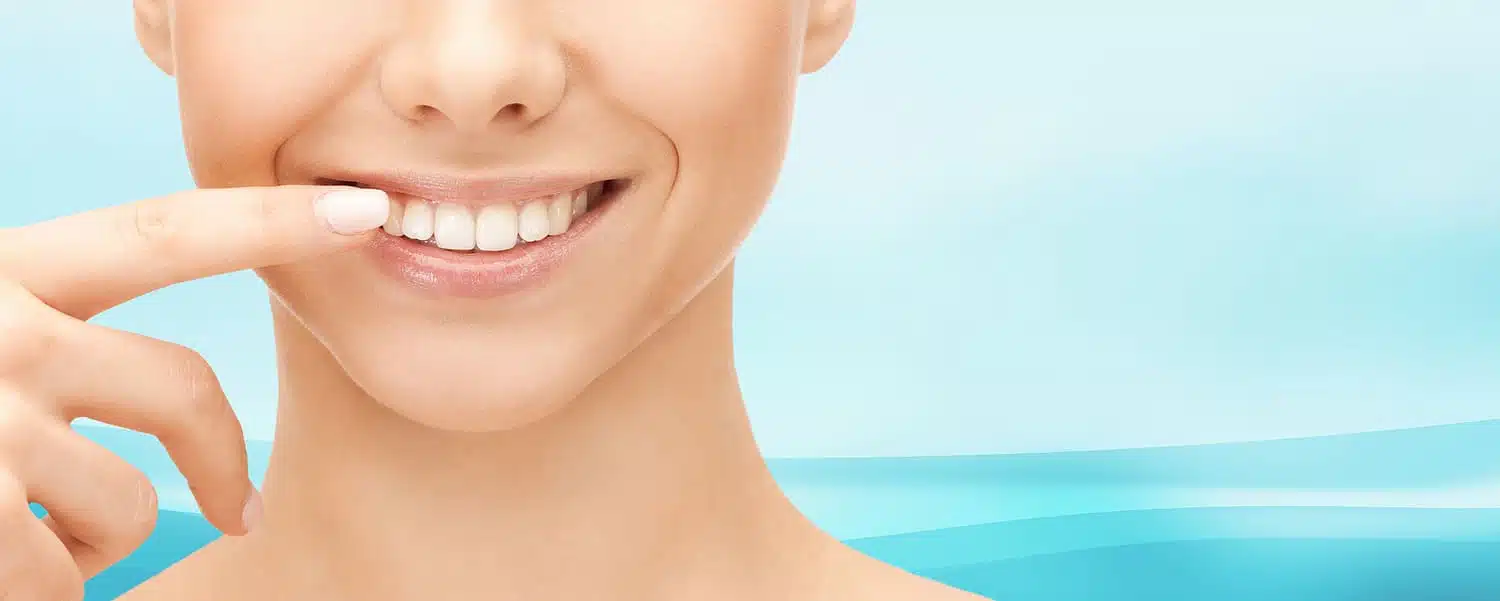 Smiling woman pointing at her teeth, showcasing a straight smile, representing adult orthodontic treatment options for improved dental aesthetics and health.