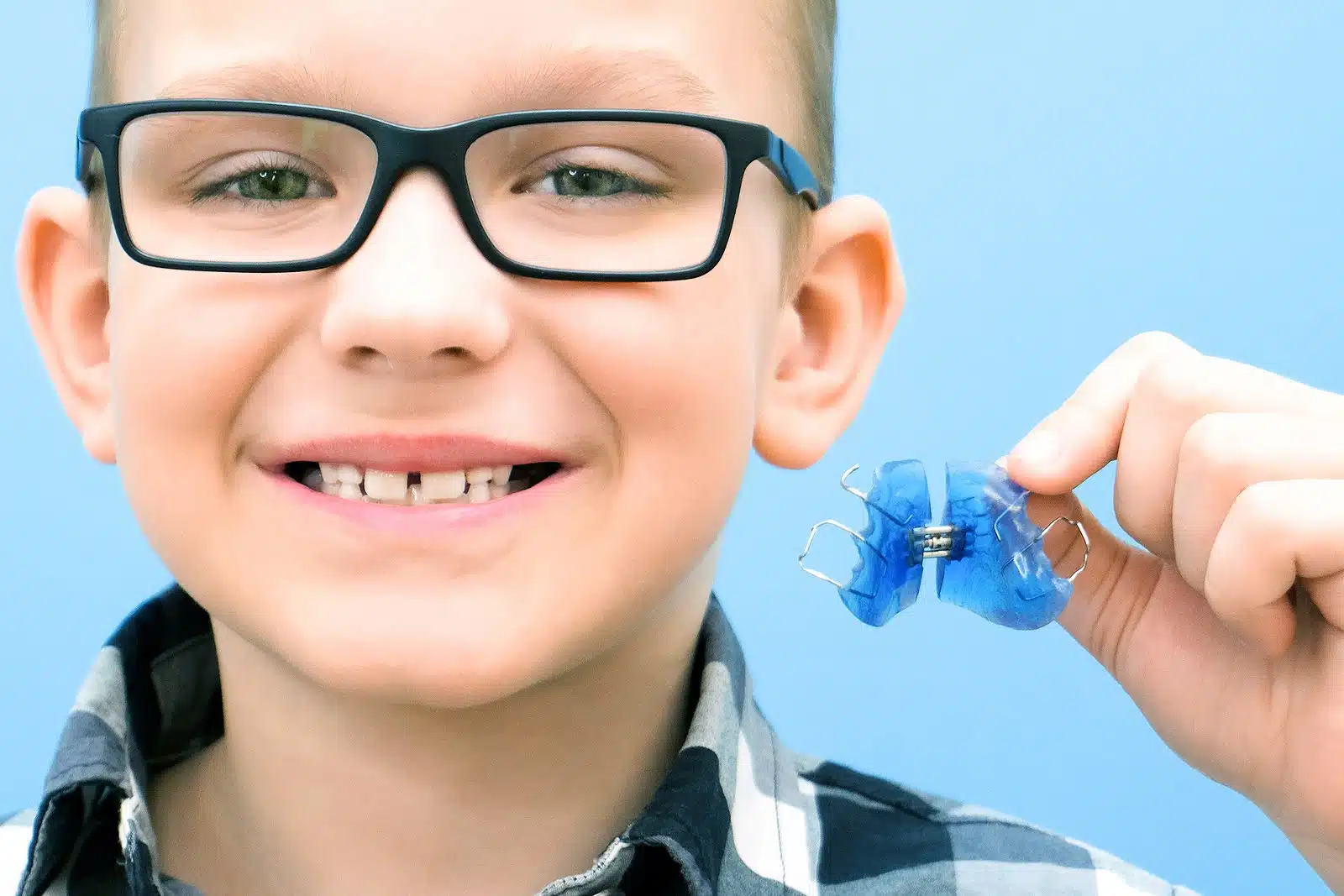 Child smiling and holding a blue orthodontic expander, illustrating pediatric orthodontic care and early dental development.
