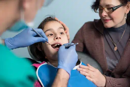 Child receiving dental examination from orthodontist, mother observing, emphasizing early orthodontic checkups for healthy dental development.